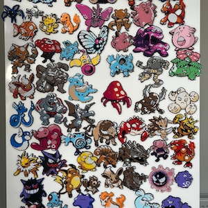 May include: A collection of numerous colourful pixel art figures crafted from plastic beads, depicting various fictional creatures in diverse poses, colours, and shapes, arranged across a plain white surface in a grid-like display.