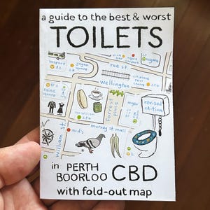 Puede incluir: Una guía de los mejores y peores baños en Perth, Australia Occidental. La guía presenta un mapa del centro de la ciudad con varias ubicaciones marcadas, incluyendo una parada de autobús, una plaza, un bar, un aparcamiento, un centro de descanso y un centro comercial. El mapa también incluye un símbolo de baño con el texto "edición revisada".