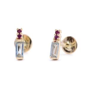 May include: A pair of gold earrings with a light blue rectangular gemstone and two small red gemstones on top.