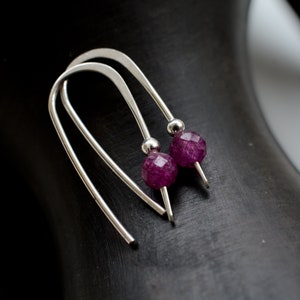 Può includere: Un paio di orecchini d'argento con un piccolo gioiello sfaccettato di colore viola scuro su ogni orecchino.