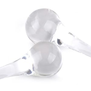 Puede incluir: Dos rodillos faciales de vidrio transparente con extremos redondos y lisos. Los rodillos están conectados a un mango transparente y liso.