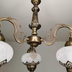 May include: A brass chandelier with three white frosted glass shades. Each shade has a decorative metal heart hanging from it.