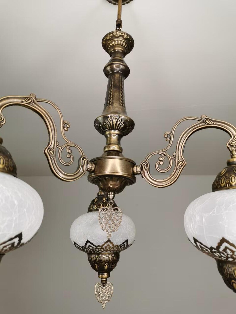 May include: A brass chandelier with three white frosted glass shades. Each shade has a decorative metal heart hanging from it.