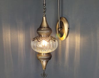 May include: A gold-toned wall sconce with a clear glass globe shade. The sconce has a decorative metal design and a chain hanging from the top.