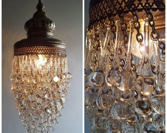 May include: A brass chandelier with a cascading design of clear glass teardrop crystals. The chandelier has a traditional design with a round, ornate top and a metal frame.
