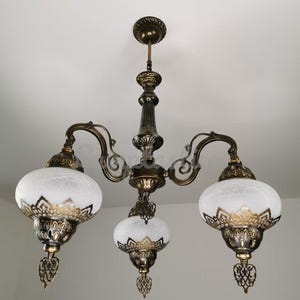 May include: A three-light chandelier with a brass finish and white frosted glass shades. The shades have a decorative gold trim and a floral pattern.