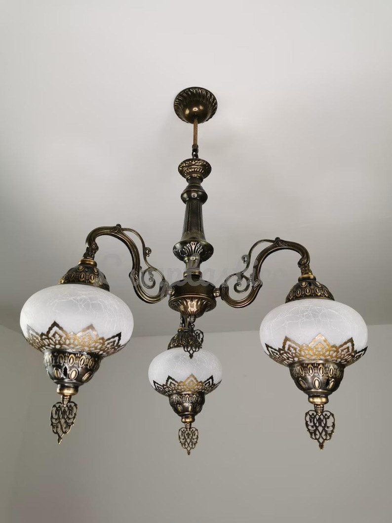 May include: A three-light chandelier with a brass finish and white frosted glass shades. The shades have a decorative gold trim and a floral pattern.