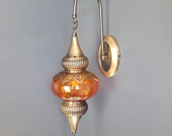 May include: A wall-mounted amber glass lamp with a decorative metal frame and a chain hanging from the top. The lamp has a traditional Moroccan design.
