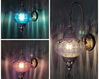 May include: Three Turkish wall sconces with ornate metalwork and glass shades. The shades are clear, teal blue, and pink.