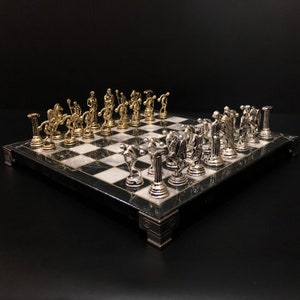 May include: A black and white marble chessboard with gold and silver chess pieces. The chess pieces are sculpted in the style of ancient Greek statues.