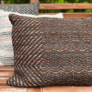 May include: A brown, black, and orange patterned throw pillow with a chevron design. The pillow is made of a soft, textured fabric.