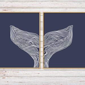 May include: Two framed prints with a navy blue background and white line drawings of a whale tail. The prints are side by side and the whale tail is split between the two.