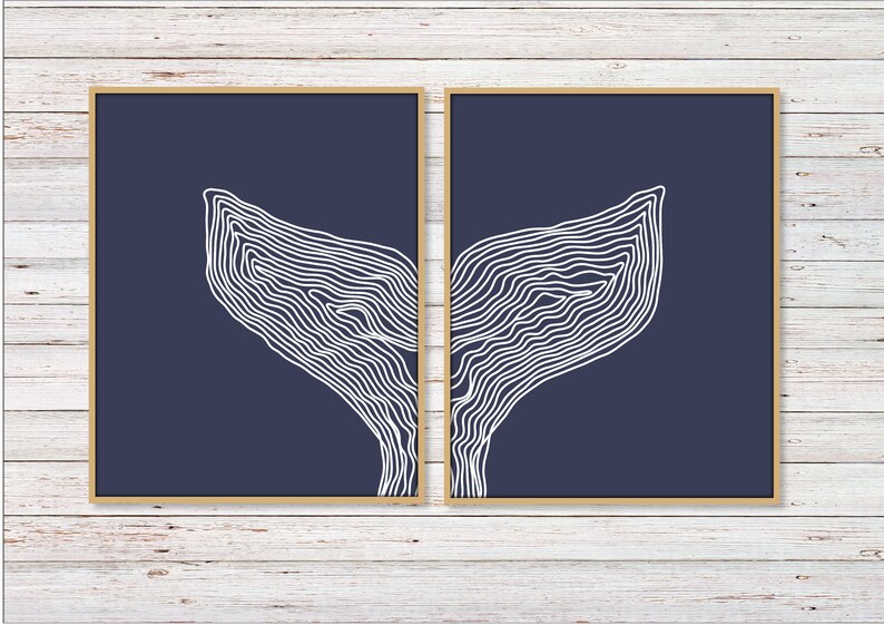 May include: Two framed prints with a navy blue background and white line drawings of a whale tail. The prints are side by side and the whale tail is split between the two.