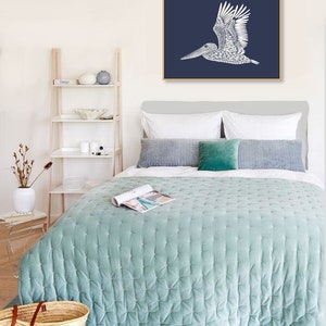 May include: A bedroom with a light blue quilted bedspread, a white headboard, and a framed print of a white pelican on a dark blue background. The print is hanging above the bed.