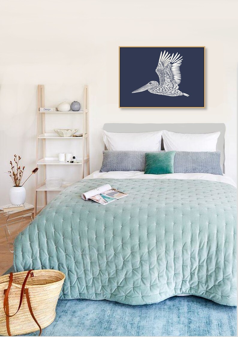 May include: A bedroom with a light blue quilted bedspread, a white headboard, and a framed print of a white pelican on a dark blue background. The print is hanging above the bed.