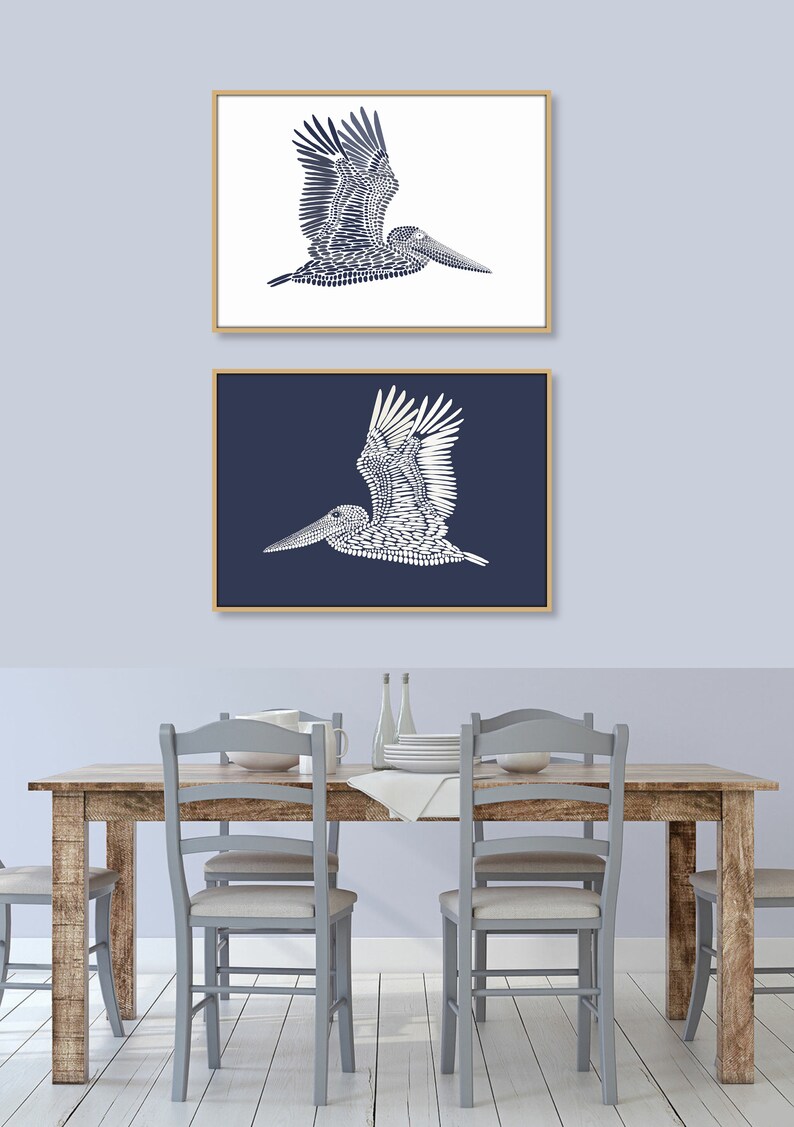 May include: Two framed prints of a white pelican silhouette against a blue background. The top print has a white background and the bottom print has a dark blue background.