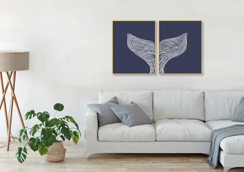 May include: Two navy blue framed prints with a white line drawing of a whale tail on each print.