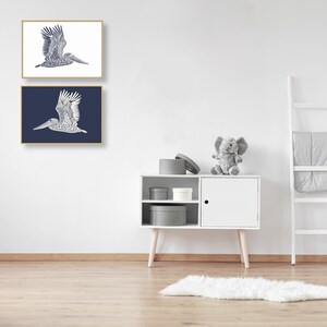 May include: Two framed prints of a blue and white stylized illustration of a pelican in flight. The top print has a white background and the bottom print has a dark blue background.