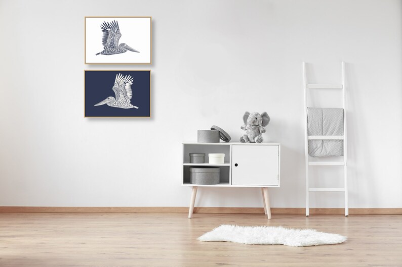 May include: Two framed prints of a blue and white stylized illustration of a pelican in flight. The top print has a white background and the bottom print has a dark blue background.