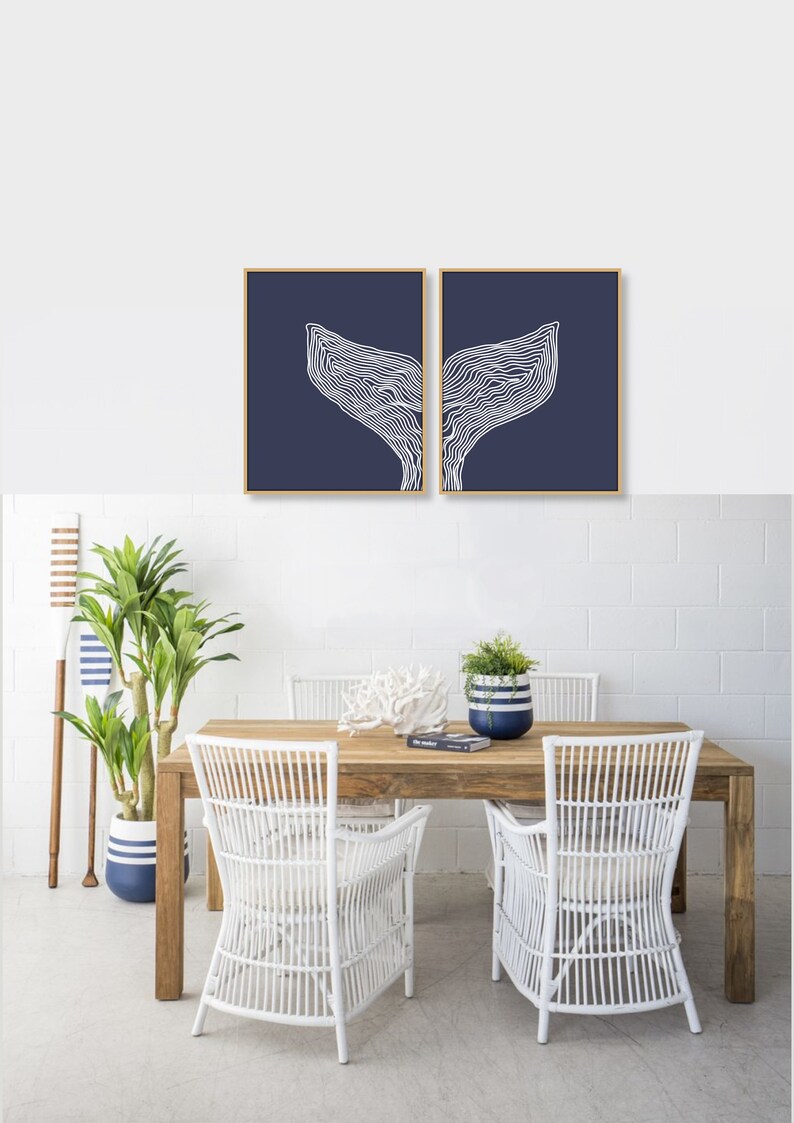 May include: Two framed prints of white whale tail silhouettes on a navy blue background. The prints are hanging on a white brick wall above a wooden table with white wicker chairs.