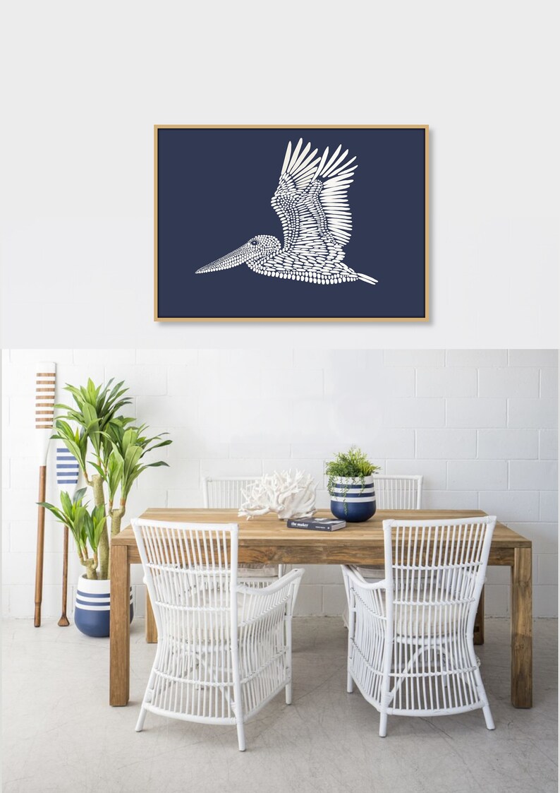 May include: A white pelican silhouette on a dark blue background, framed in wood. The pelican is made up of small white dots. The image is hanging above a wooden table with white wicker chairs.