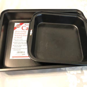 May include: Two black rectangular baking pans with a nonstick finish. The larger pan features a product label with the text "Heavy Gauge, Professional Nonstick Finish on Steel!" and dimensions of 16 inches by 11.5 inches by 2 inches.