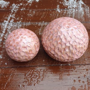 Op de afbeelding: Twee getextureerde, bolvormige objecten met een roodbruine tint. De bollen hebben een gesneden patroon en liggen op een houten oppervlak. De grotere bol heeft een diameter van ongeveer 15 cm, de kleinere ongeveer 10 cm.