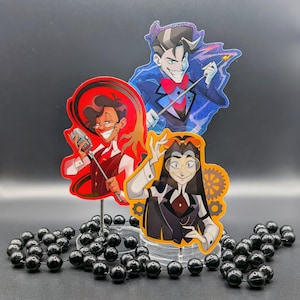 Op de afbeelding: Drie gestanste stickers met gestileerde stripfiguren. Eén personage houdt een microfoon vast tegen een rode achtergrond, een ander draagt een blauw pak met een rode vlinderdas en de derde heeft lang donker haar met oranje tandwielmotieven.