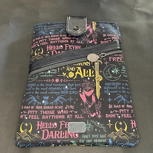 May include: Black clutch bag with a flap and zip pocket. The patterned design features colourful text and illustrations, including the words "Hello Feyre Darling". The bag has a silver-toned metal zipper pull.