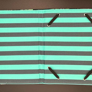 May include: A teal and grey striped fabric photo album with black elastic straps and a grey fabric strap.