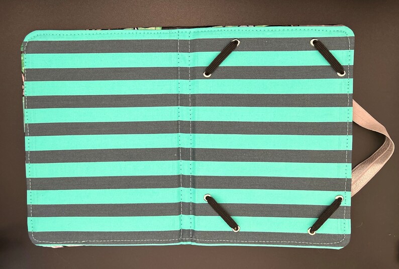May include: A teal and grey striped fabric photo album with black elastic straps and a grey fabric strap.