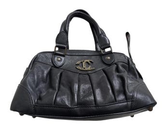 Pode incluir: Bolsa de mão de couro preta com design frontal franzido e alças superiores duplas. A bolsa apresenta um emblema dourado na frente e uma pequena alça lateral. A bolsa é um estilo clássico.