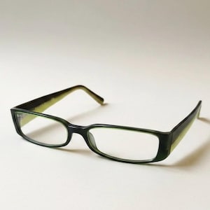 May include: A pair of rectangular spectacles featuring a dark green outer frame and a contrasting light lime green inner frame. The glasses have thin, straight temples and a standard bridge, showcasing a two-tone colour scheme throughout the design.