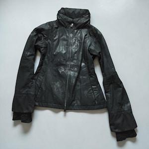 May include: A black jacket with a high collar and a full-length front zipper. The garment features a subtle, mottled, or distressed finish across the fabric, long sleeves with fitted cuffs, and two zippered pockets located at the waist area.