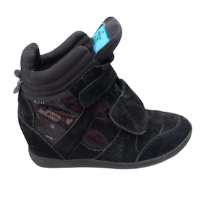May include: Black suede wedge sneakers with a zipper detail and a mesh panel. The sneakers have a velcro strap closure and a platform sole.