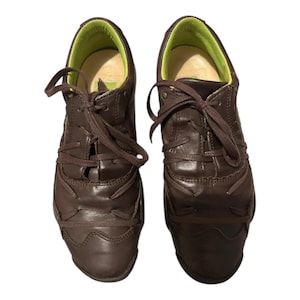 May include: A pair of brown leather lace-up shoes with a green lining. The shoes have a unique design with a series of overlapping leather panels.