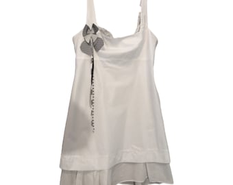 May include: White sleeveless dress with a layered skirt and a gray flower embellishment on the bodice.