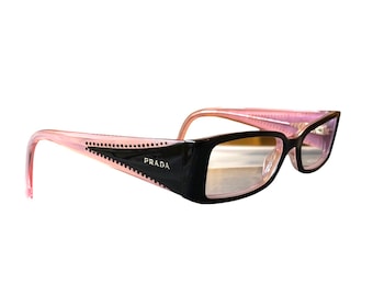 May include: Black and pink Prada eyeglasses with a rectangular frame. The temples are pink with small dot details and the Prada logo is visible on the black frame. The lenses are clear.