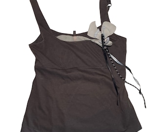 May include: A dark brown sleeveless tank top with a decorative flower detail on the left shoulder. The flower is made of a light gray fabric with black and white accents.
