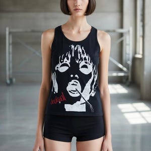 May include: Black tank top with a white graphic face design and the word "desigual" in red. The tank top is paired with black shorts. The image is taken in a studio setting.