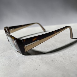 Könnte beinhalten: Sonnenbrille mit Schildpattmuster und rechteckiger Rahmenform. Die Bügel haben ein zweifarbiges Design mit einem dunkelbraunen Schildpatt-Oberteil und einem beigen Unterteil, wobei das Prada-Logo an der Seite aufgedruckt ist.