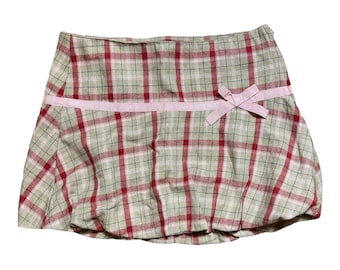 May include: A plaid skirt with a pink bow at the waist. The skirt is made of a light-weight fabric and has a gathered look.