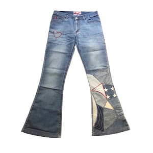 May include: Light blue denim jeans with a flared leg. The jeans feature a red embroidered heart on the front pocket and a patchwork design on the lower leg with stars and stripes.
