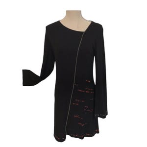 Peut inclure: Robe noire à manches longues avec un détail de fermeture éclair diagonale et du texte rouge sur le devant. Le texte comprend des chiffres et des mots comme "tasse" et "recette".