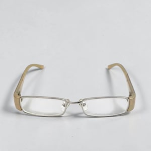 May include: Eyeglasses with rectangular lenses and a silver frame. The temples are a light tan colour. The glasses are set against a plain white background.