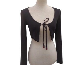May include: A dark brown cropped cardigan with long sleeves and a tie at the front. The tie has two red tassels.