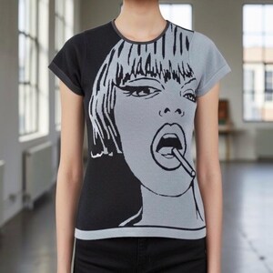 May include: A black and gray short-sleeved t-shirt featuring a pop art style graphic of a woman smoking a cigarette. The graphic is split, with the left side black and the right side gray. The shirt has a round neckline.