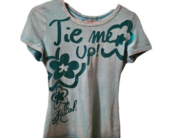 May include: A light blue t-shirt with a teal graphic that says "Tie me Up!" and a flower design. The shirt also has the word "Killah" written in teal.