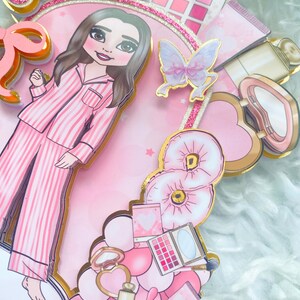 Personalized makeup-themed cake topper featuring a girl in pink striped pajamas surrounded by beauty and spa accessories including makeup brushes, lipstick, blusher, eyeshadow, skincare items, and a pink bow. The topper is decorated in pink glitter card and gold mirror  with the name and age of the birthday girl, making it perfect for a glam birthday, spa party, or makeup-themed celebration.