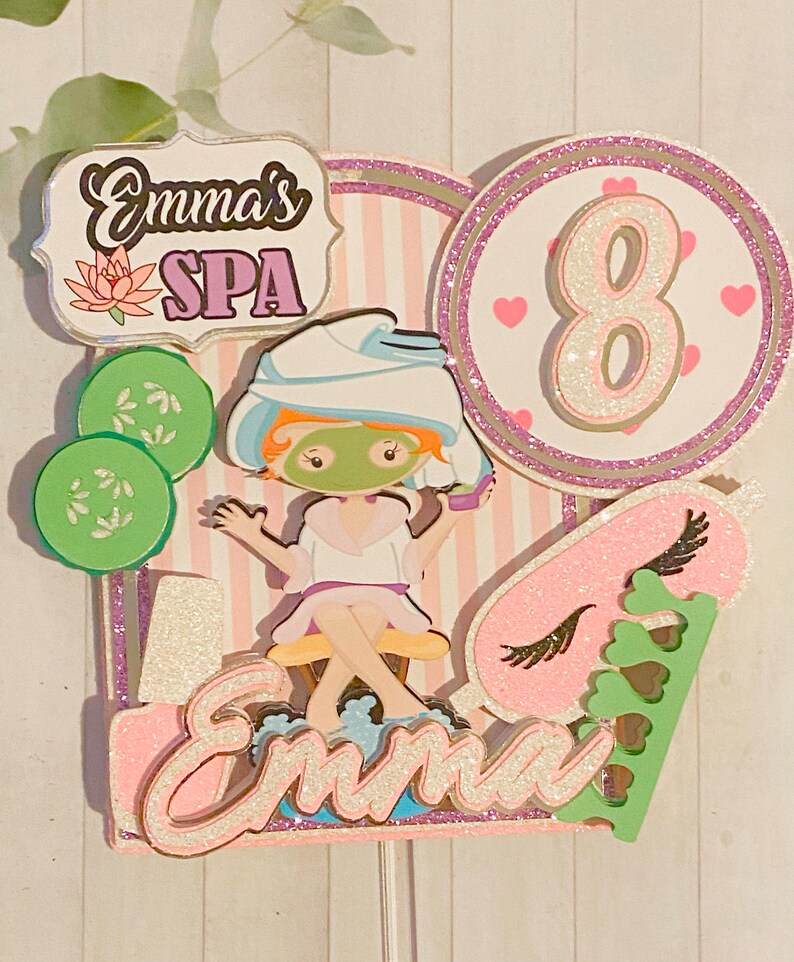 Puede incluir: Adorno para tarta con tem&aacute;tica de spa con el texto "Emma's SPA" y una figura de dibujos animados con mascarilla. El adorno incluye el n&uacute;mero 8, rodajas de pepino y el nombre "Emma". El dise&ntilde;o presenta colores rosa, verde y blanco.